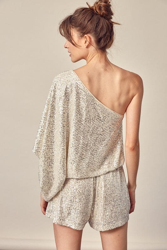 This silver party romper is sure to catch a few double-takes with the glistening sequins and attractive silhouette. The cinched natural waist with tie flatters the figure. The draped shoulder style shows off some skin while balancing the billowy sleeves.