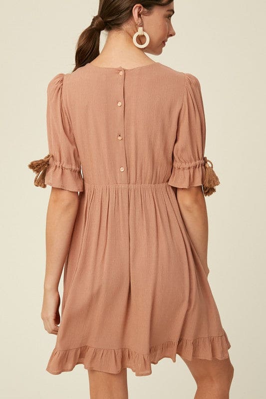 Our round-neck babydoll dress by Listicle featuring puffed sleeves with elastic cuffs with cord accent, back buttoned closure and a full, flirty ruffled hem. Wear as is, or add definition to the elasticized waist using a fashionable belt. This signature style is crafted from textured woven fabric, fully lined and is cut to a flattering loose fit for a playful yet sophisticated look.Rear view shows a four button closure. www.hoytietoytie.com
